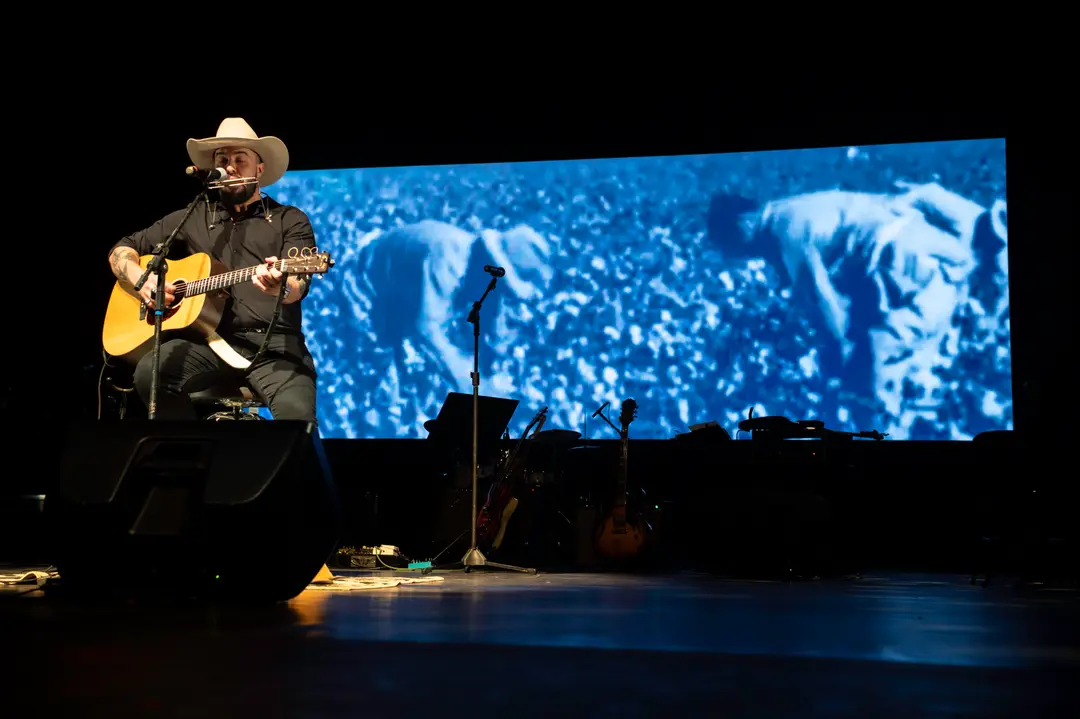 Augusto Bon Vivant ao vivo no palco, com violão e gaita de boca